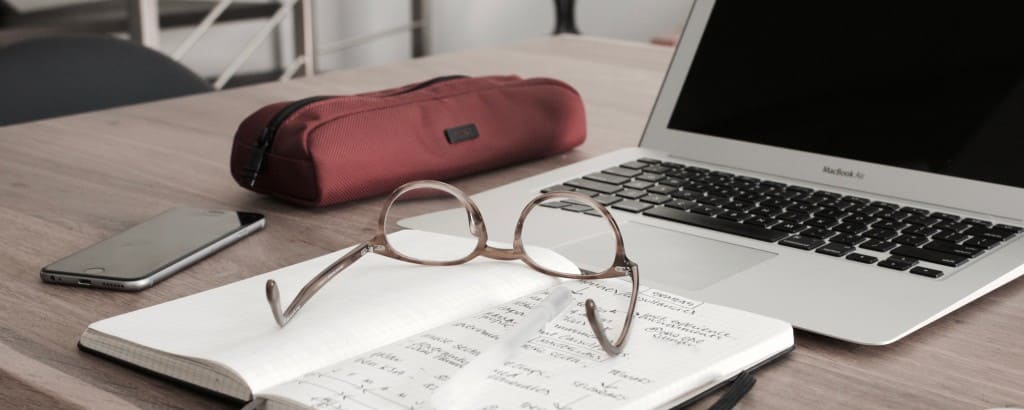glasses on a notebook near a computer and cell phone