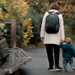 a mother walking with her toddler, she is wearing a backpack implying she is a student