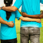 four diverse students standing with their arms linked on each others' backs to symbolize a team