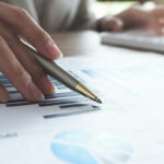 A woman's hand holding a pen seemingly reviewing charts and graphs.