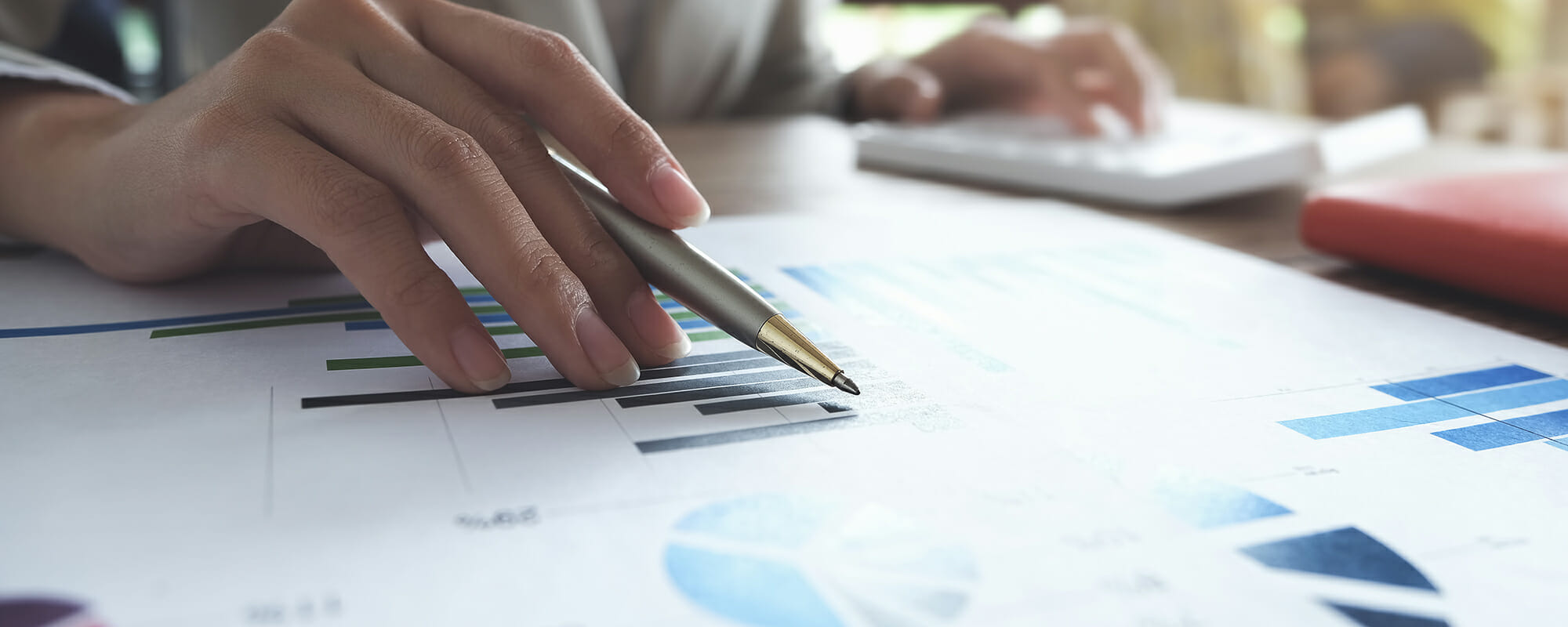 A woman's hand holding a pen seemingly reviewing charts and graphs.