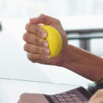 Stressed office worker with anti stress ball types email